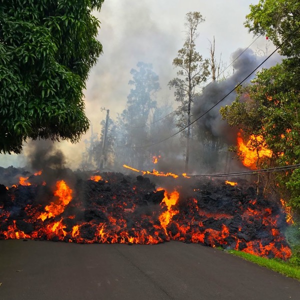 molten lava flowing down a street burning grass and trees