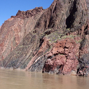 A canon wall of reddish brown rock along a river