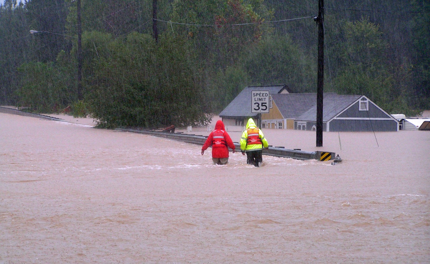 2 workers standing knee and thigh deep in flood waters measuring the height