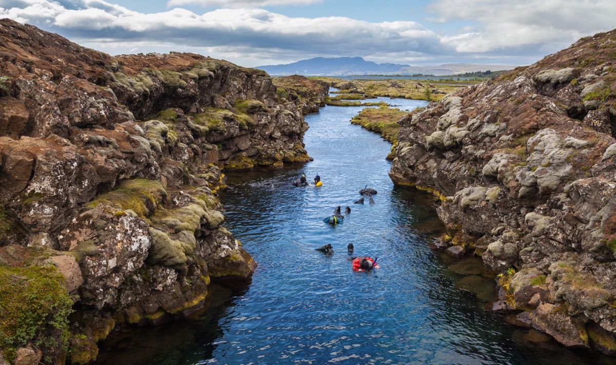 people in multicolered wetsuits snorkling between to large rock formations