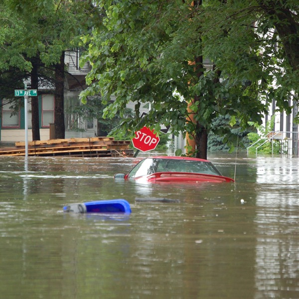 a car floating in a floaded street. Around it are a tilted stop sign and floating debris