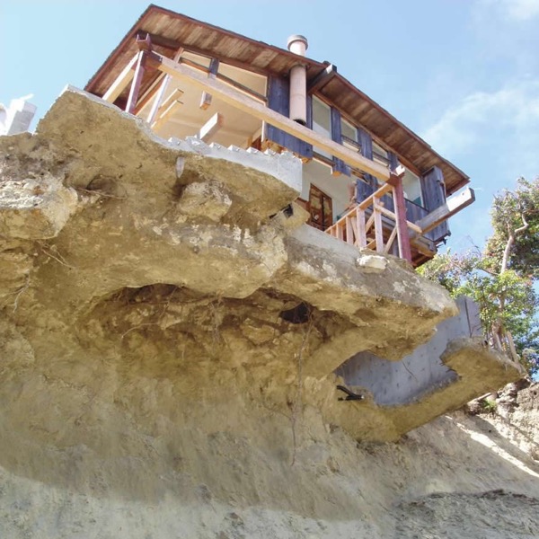 A house teetering on the edge of a cliff, where the landhas slid out from under it