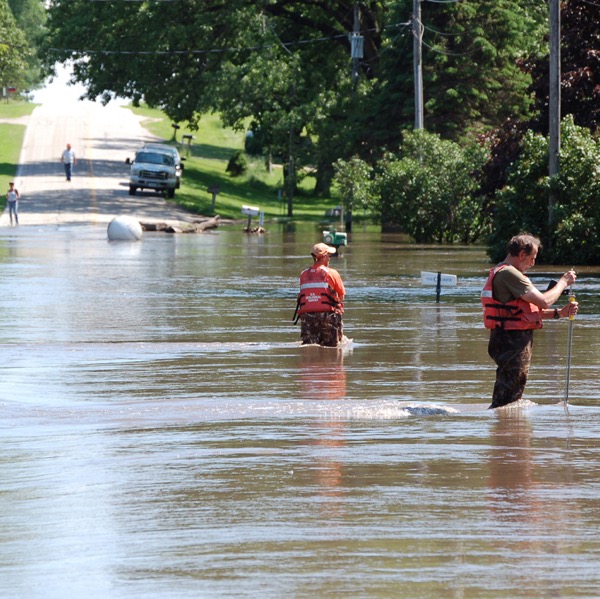two men measure flood levels in a flooded street