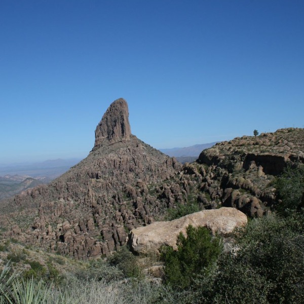 A tall weathered rockfomation at the top of a hill surrounded by smaller volcanic rocks and green vegetation