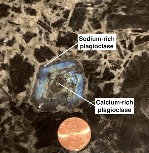 “Zoning” in a large crystal of plagioclase formed during the slow cooling of magma in an intrusive igneous body. The most calcium-rich concentration is located in the center that formed during the early cooling stages. The plagioclase became progressively more sodium-rich as cooling and crystal growth continued. The blue coloration is called “schillerization” due to microscopic inclusions common to this variety of plagioclase. Photo by Shelley Jaye.