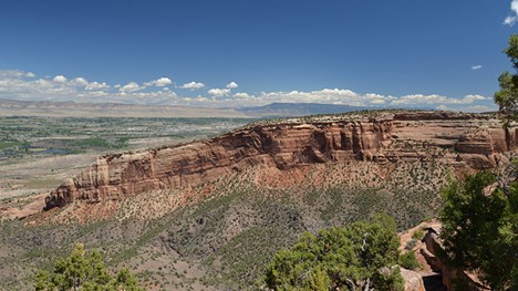 A photograph of a landscape in Colorado: a big cliff changes the angle of its strata from horizontal to slightly tilted at the left. Below the cliff is a layer of orange/tan shale, and below that a purple unit.