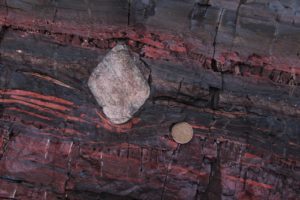 Photo of an outcrop of rock showing a dropstone of quartzite in banded iron formation.