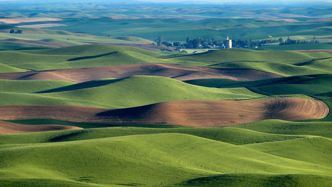 Aerial photograph of grass-covered rolling hills, with a small farm in the distance.