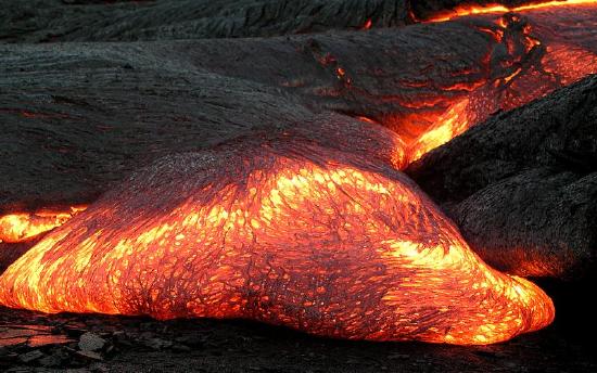 Orange lava flows as a black crust forms on its surface as it cools.