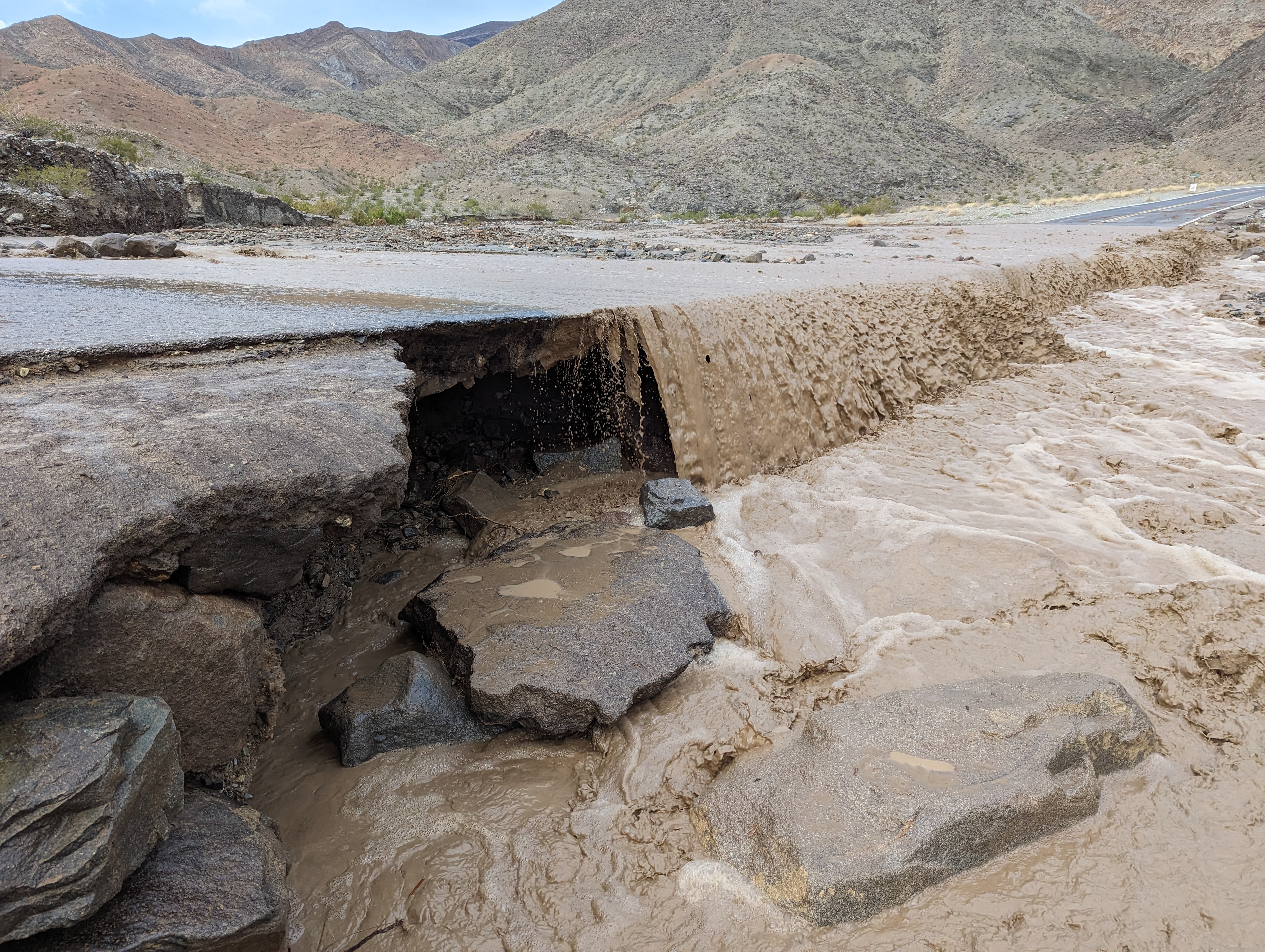 After heavy rain in the area, muddy flood water flows over a road.