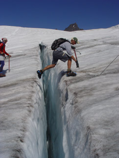 A person crosses over a large, deep crack in a glacier.