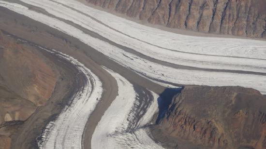 Two glaciers which look like roads covered with ice have dark brown stripes of sediment down the middle and along the edges.