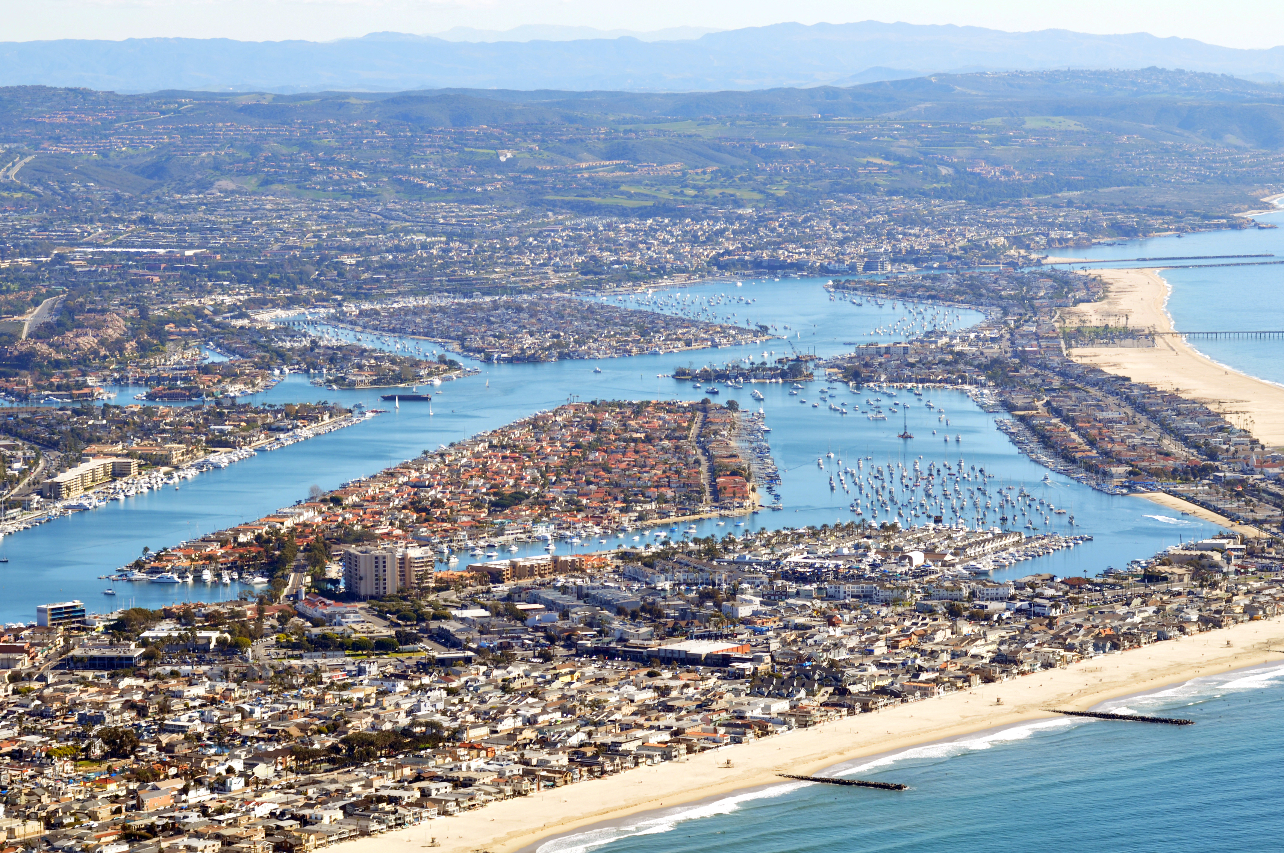 Aerial view of a coastal city and suburbs around a harbor with mountains in the background.