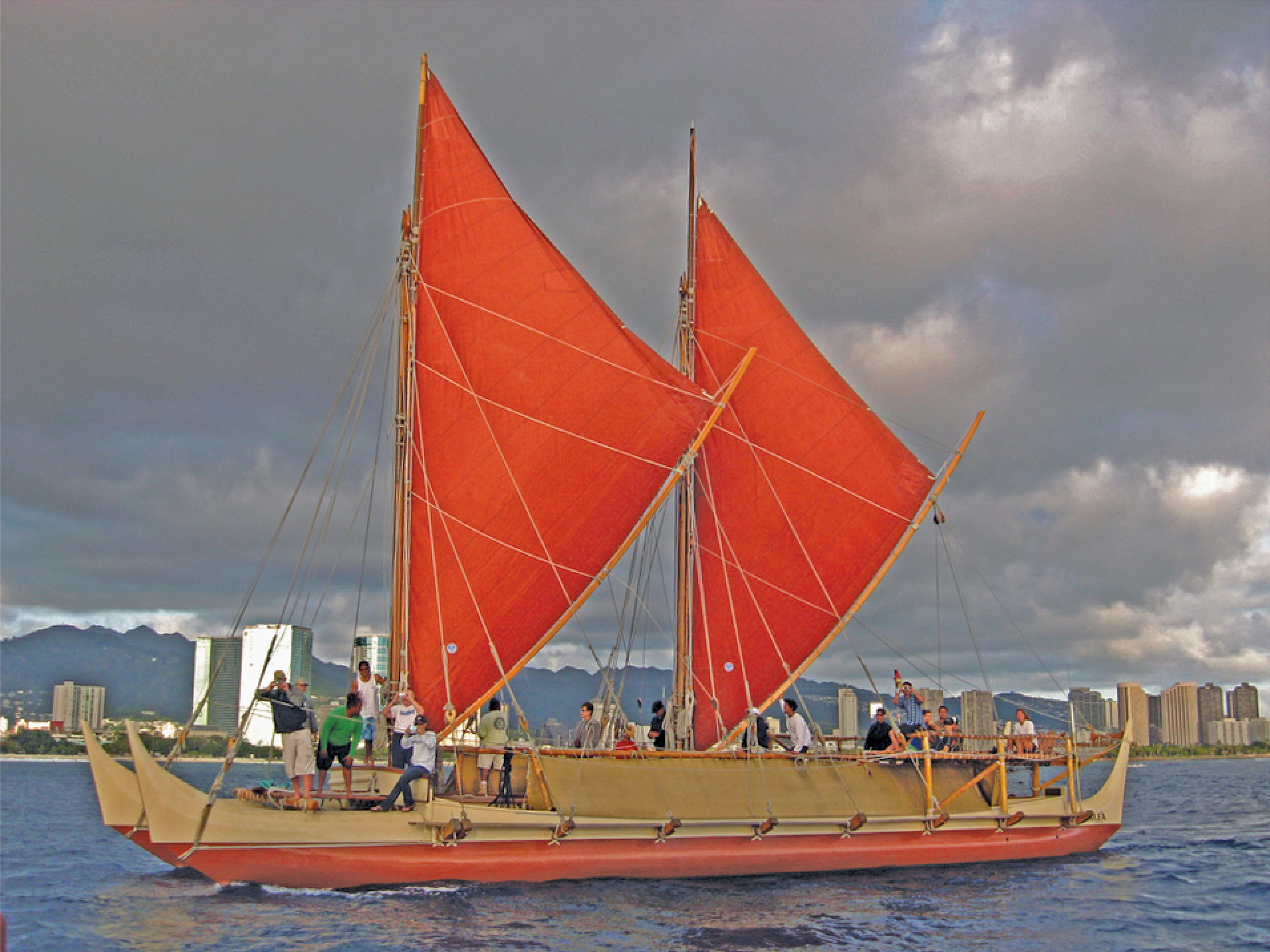 A large, double-hulled sailing canoe with bright red triangular sails