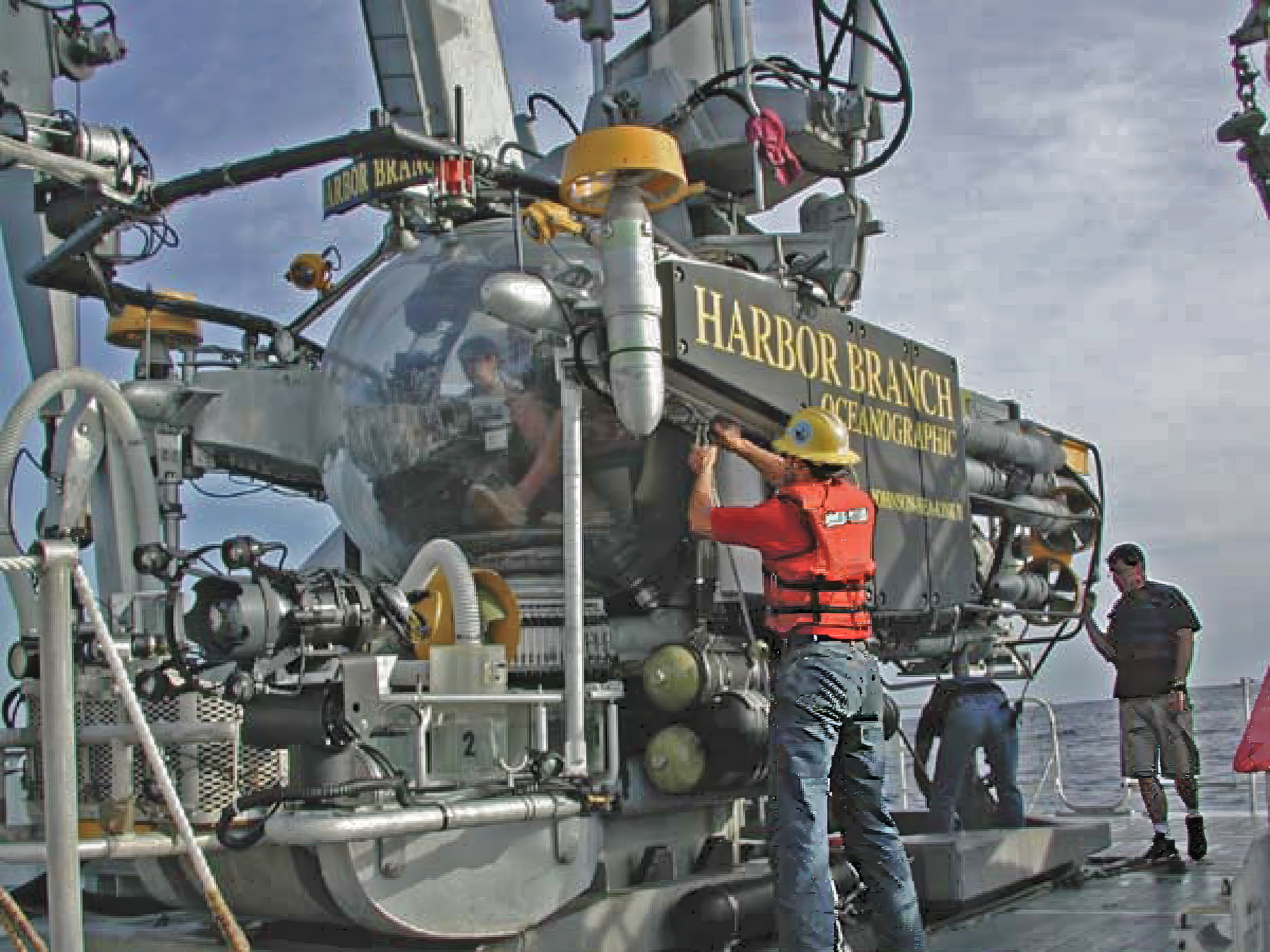 Three people working on a sled-mounted submersible with another person in a large viewing bubble on the front.