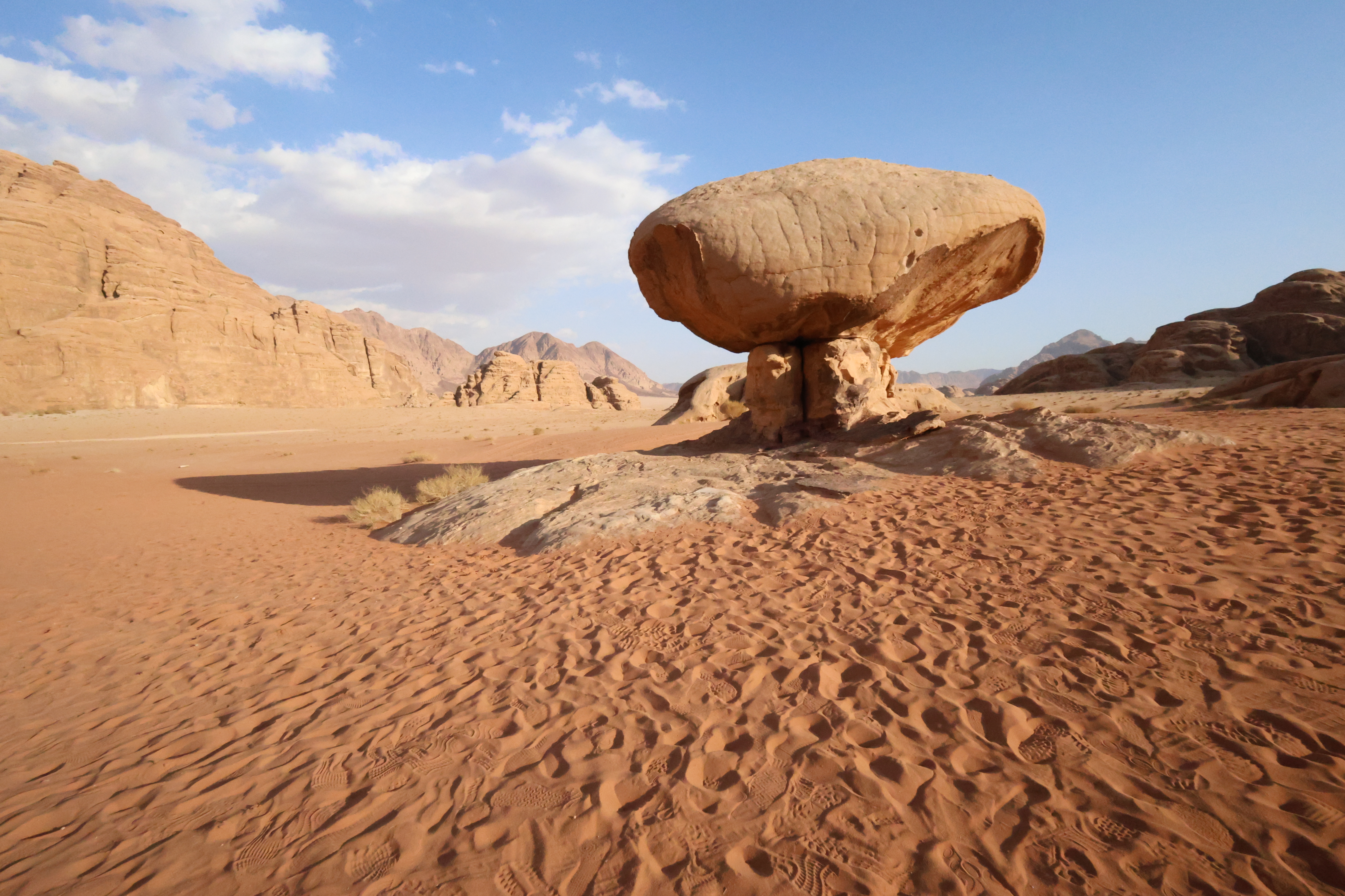 A large, mushroom-shaped rock pedestal standing on rippled sand in a vast desert landscape.