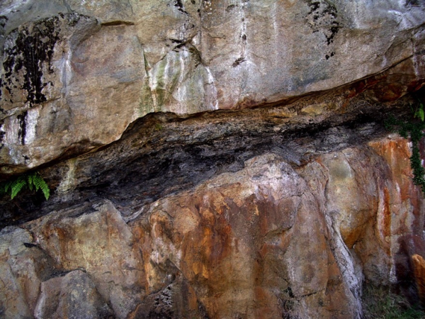 A tall, light colored rock wall with a black streak running through the middle.