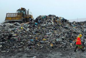 A pile of garbage at a landfill and a large bulldozer in the background