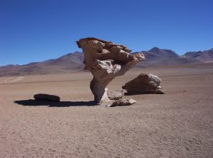 Large rock standing on a narrow base sandblasted by saltating sand blowing near the ground.
