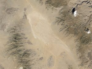 Satellite image of desert dry lake or playa surrounded by mountains.