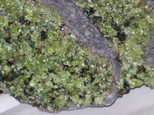 Many small crystall of the green mineral olivine in a mass of basalt